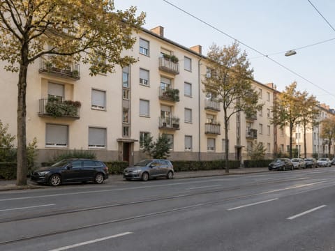 Wohnblock der Nachkriegszeit mit Balkonen an einer breiten Straße mit Straßenbahngleisen
